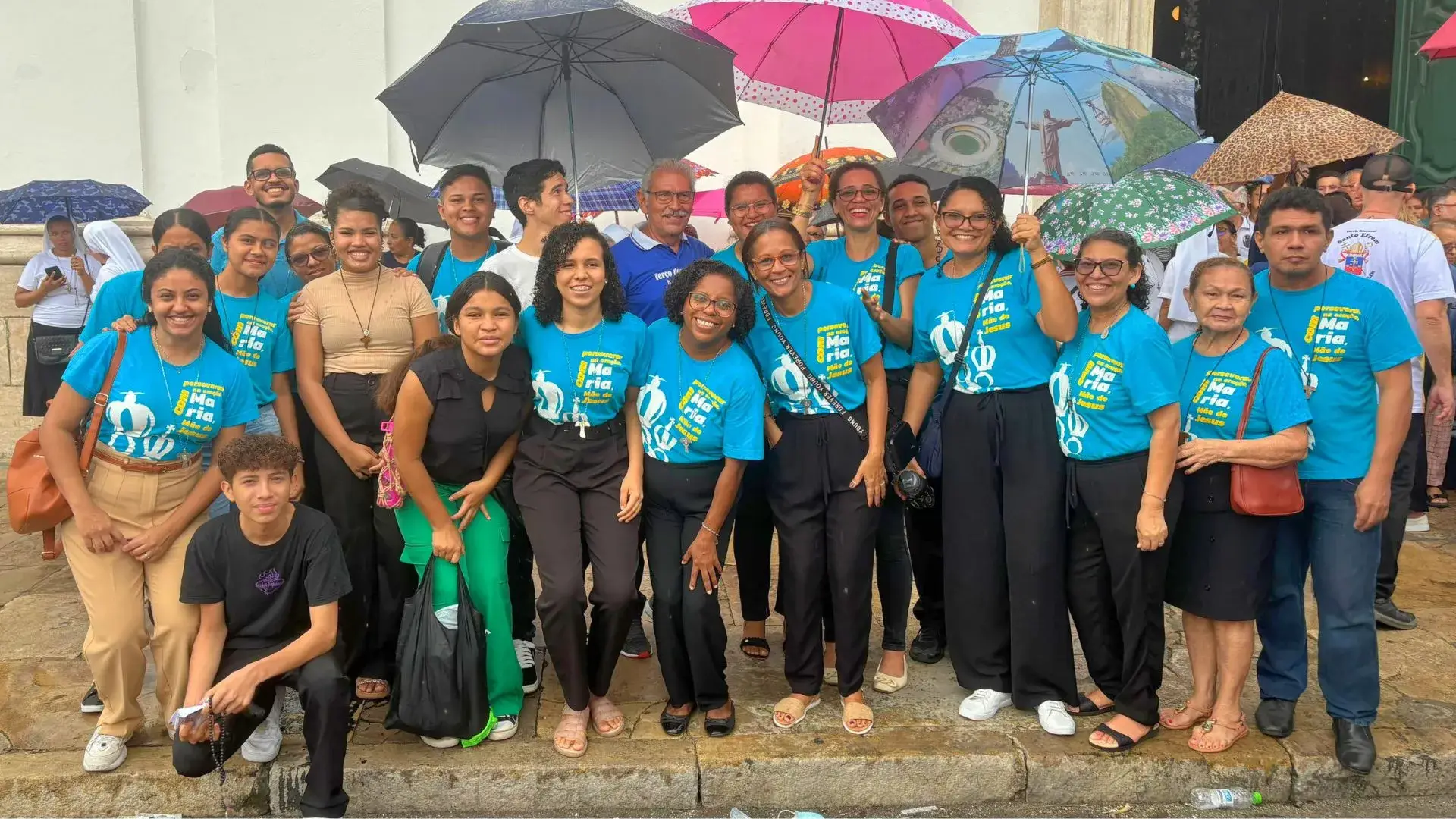 Diversos membros da Comunidade Maíra reunidos na frente da Catedral Metropolitana de Belém vestindo camisas azuis, cada uma segurando um guarda-chuva, criando uma cena vibrante.